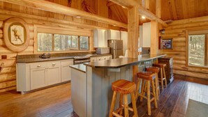 A log cabin kitchen with wooden walls, a central island with stools, and a large window.