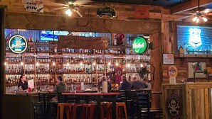 A bar with wooden decor, multiple liquor bottles, and patrons seated at tables. - Renovated 1912 Home 2B/2B w/King&Queen fenced yard (Grants Pass)