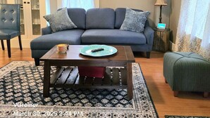 A living room with a blue sofa, a wooden coffee table, a patterned rug, a cabinet, and a wall with framed photos. - Renovated 1912 Home 2B/2B w/King&Queen fenced yard (Grants Pass)