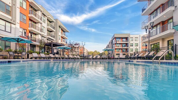 A swimming pool surrounded by modern apartment buildings with balconies and lounge chairs. - Landing | Chic 2BD, Clubhouse, Game Room (Atlanta)
