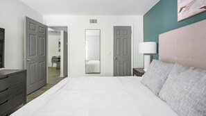 A hotel room with a large bed, a bedside table with a lamp, a dresser, and a mirror.