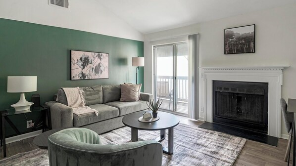 A living room with a green wall, a fireplace, a sofa, a coffee table, and a side table with a lamp.