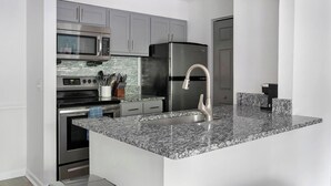 A modern kitchen with stainless steel appliances, granite countertops, and grey cabinetry.