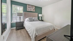 A bedroom with a bed, nightstands, a window with blinds, and a painting on the wall.