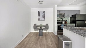 A modern kitchen with grey cabinets, a stainless steel refrigerator, and a microwave. There is a dining area with a round table and two chairs.