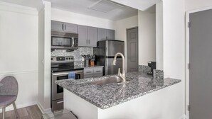 Une cuisine moderne avec des meubles gris, des appareils en acier inoxydable et un plan de travail en granit.