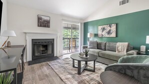 Un salon moderne avec une cheminée, un mur d’accent vert et une vue dégagée sur l’extérieur grâce à une porte-fenêtre coulissante.
