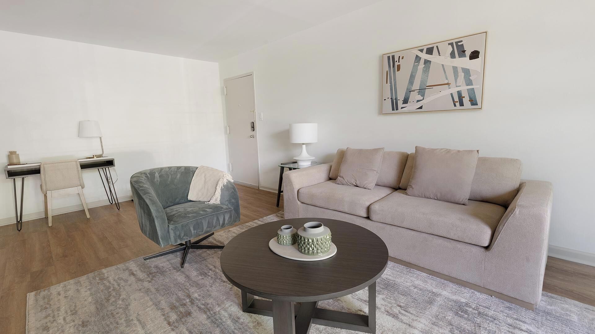 Una sala de estar moderna con un sillón gris, un sofá beige y una mesa de centro redonda con adornos.