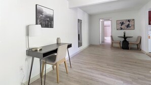 A modern living room with a wooden floor, a dining area with two chairs and a table, and a desk with a chair.