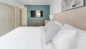 A neatly arranged hotel room with a bed, a dresser, a television, and a framed artwork on the wall.