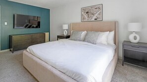 Quarto com uma cama grande, cômoda, televisão e duas mesas de cabeceira com abajures.