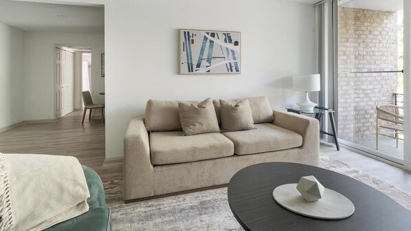 Uma sala de estar moderna com um sofá bege, uma mesa de centro redonda e uma obra de arte contemporânea na parede.