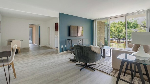 A modern living room with a dining area, a grey armchair, a sofa, and a TV mounted on the wall.