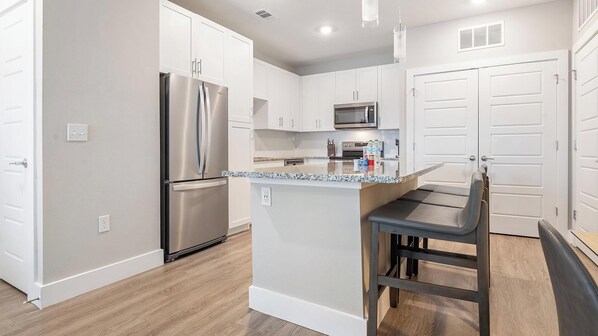 Una cocina moderna con armarios blancos, un refrigerador de acero inoxidable, un microondas y una barra con taburetes.