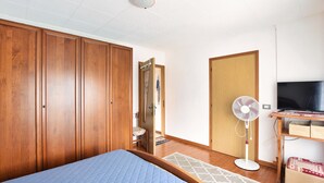 A bedroom with a bed, wooden wardrobe, a standing fan, a television, and a small table with a TV stand. - Lovely apartment in Pedavena with WiFi (Pedavena)