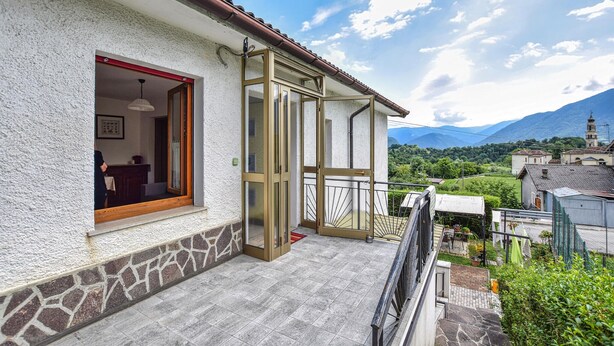 A house with a balcony, a door leading to a room, and a view of mountains in the background. - Lovely apartment in Pedavena with WiFi (Pedavena)