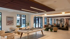 A modern indoor space with a pool table, comfortable seating, large windows, and a ceiling with linear light fixtures. - Landing | Amazing 1BD, Rooftop Lounge, Yoga Studio (Jacksonville)