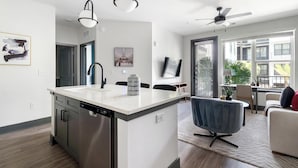 Una cocina moderna con lavavajillas, un comedor con una silla azul y un ventilador de techo.
