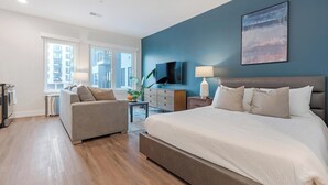 A modern bedroom with a large bed, a sofa, a TV, and a view of the city. - Landing | Amazing Studio, Clubhouse (Philadelphia)