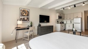 A modern bedroom with a large bed, a desk with a chair, a flat-screen TV, and a kitchenette with cabinets and appliances. - Landing at The Harrison - Studio in Northeast R... (Raleigh)