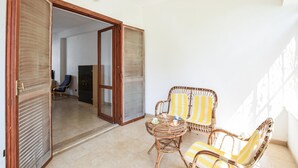 Una puerta abierta que da a una habitación con una silla y una mesa, una silla azul al fondo y un suelo de baldosas.