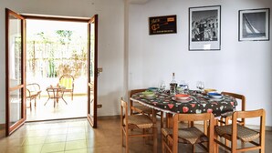 Un comedor con una mesa redonda dispuesta para cuatro personas, rodeada de sillas de madera con cojines de asiento trenzados. Se ve un cartel en la pared que dice 'BAR CERRADO'.