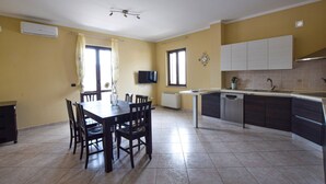Una cocina moderna con zona de comedor, que incluye una mesa grande, sillas, un televisor y un horno empotrado.