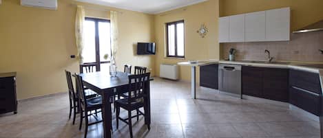 Una cocina moderna con zona de comedor, que incluye una mesa grande, sillas, un televisor y un horno empotrado.
