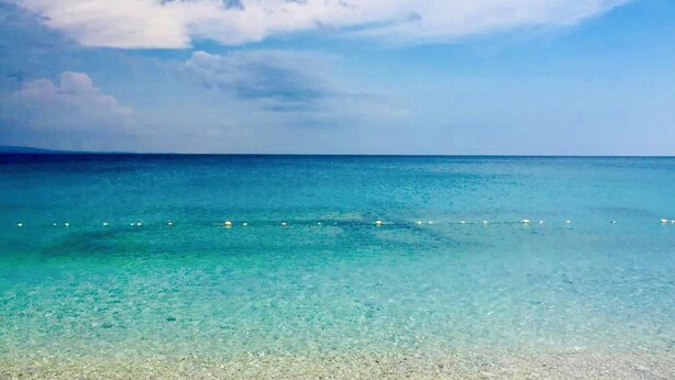 Vista despejada de una playa con aguas turquesas poco profundas y una costa distante.