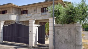 Un edificio de dos pisos con fachada de concreto, entrada protegida por una reja y un pequeño balcón.