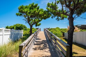 A wooden boardwalk leading to a white fence and trees.