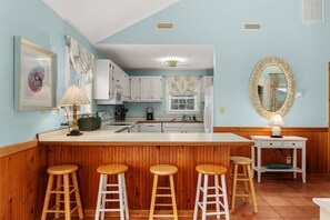Una cocina con taburetes de madera, armarios blancos y un espejo grande.