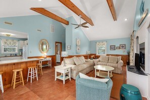 Uma sala de estar espaçosa com teto de madeira, área de cozinha com balcão e mesa de jantar com banquetas.