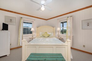 A bedroom with a bed, two bedside lamps, a ceiling fan, and a window with curtains.