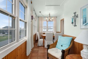 A dining area with a table and chairs, large windows, a chandelier, and a wall-mounted lamp.