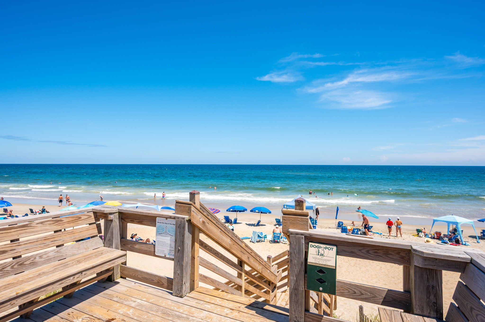 A wooden boardwalk leading to a beach with umbrellas and people.