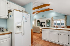 A kitchen with white cabinets, a white refrigerator, a wooden ceiling, and a dining area with a table and chairs. - "Ehh, What's up, Duck?": Private Pool, Dog-Friendly, Short Walk to Beach Access (Duck)