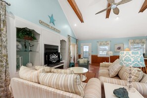 A spacious living room with striped sofas, a fireplace, and a ceiling fan.