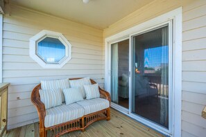 A wicker sofa with striped cushions on a wooden deck, a hexagonal window, and a sliding glass door leading to an outdoor area. - "Ehh, What's up, Duck?": Private Pool, Dog-Friendly, Short Walk to Beach Access (Duck)