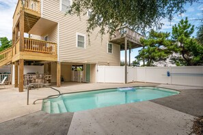 A two-story house with a wooden deck, a pool, and a covered patio area.