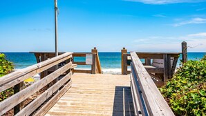 Eine Holzstege führt zu einem Strand unter blauem Himmel.