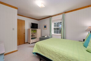 Um quarto com cama, televisão sobre uma cômoda, janela com cortinas e uma porta.