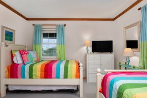 A bedroom with a bed, a dresser, a television, and a window with curtains.