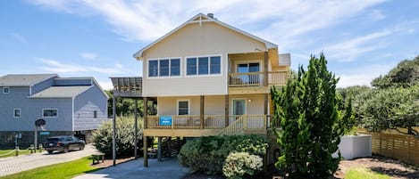 A two-story building with a balcony on the upper floor, a covered outdoor area, and a driveway leading to a parked car.
