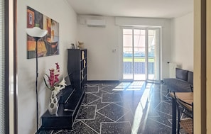 Un salon moderne avec un sol carrelé en noir et blanc, un canapé noir, une table basse, un vase avec des fleurs, un tableau au mur et une vue sur un terrain de sport par la porte vitrée.