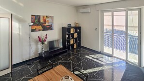 A living room with a black and white tiled floor, a wooden coffee table, a TV, a bookshelf, and a painting on the wall.