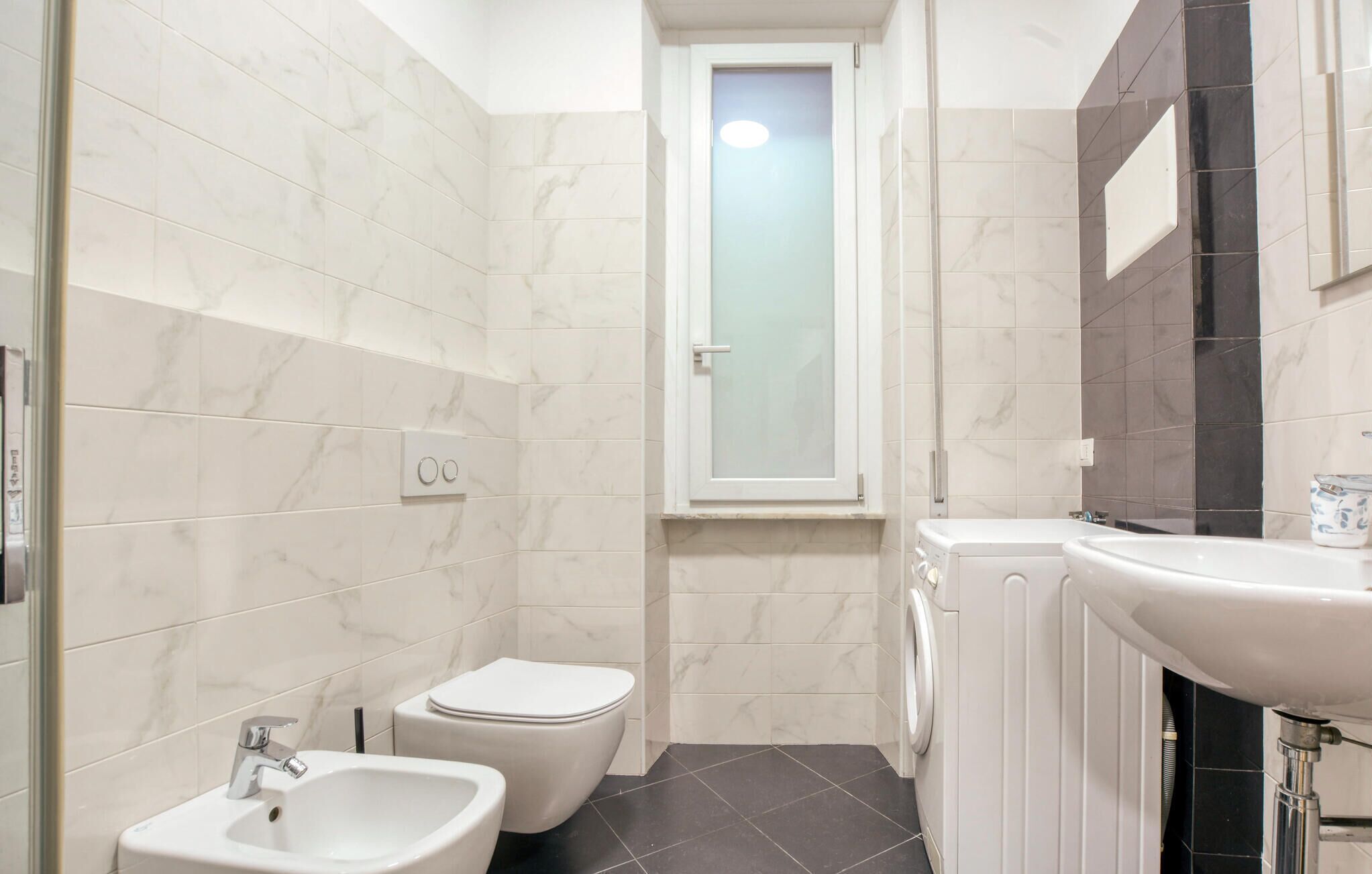 A compact bathroom with a toilet, bidet, sink, and a small window.