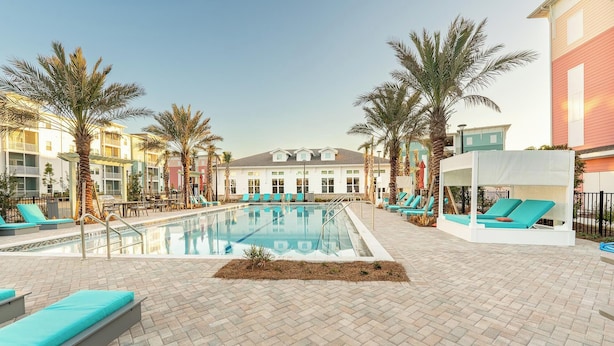 A pool area with lounge chairs and palm trees, surrounded by buildings with balconies.