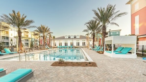 A pool area with lounge chairs and palm trees, surrounded by buildings with balconies.