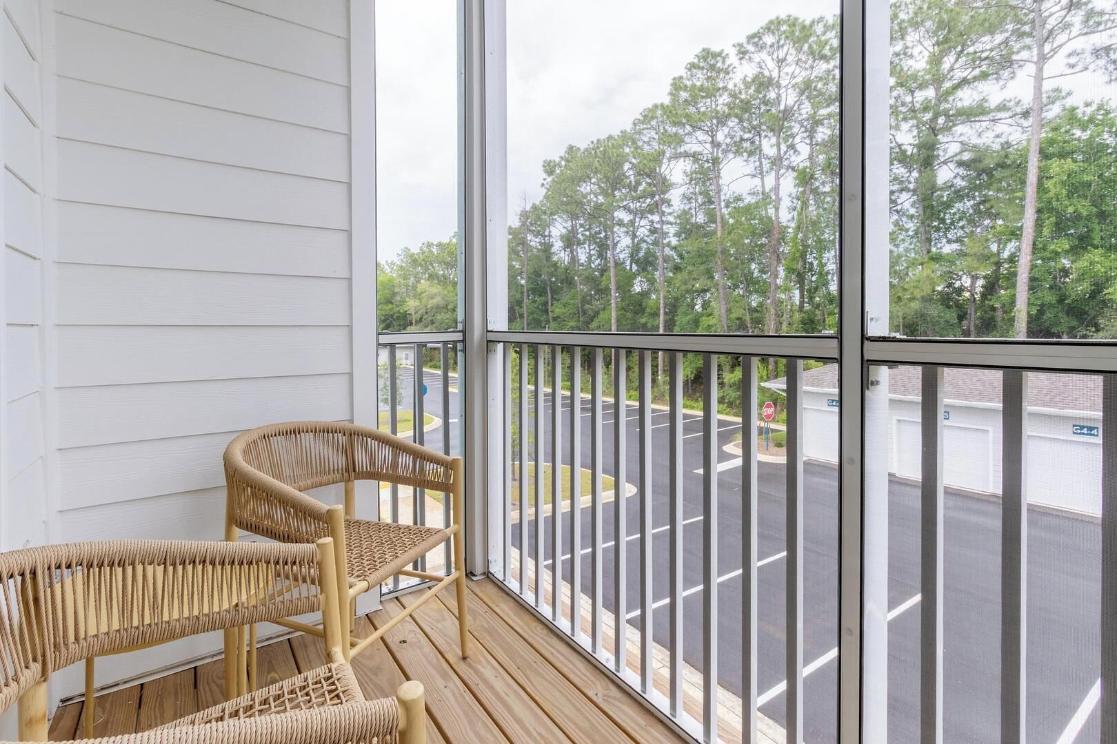 A balcony with two wicker chairs and a view of a parking lot and trees.